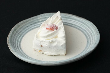 One small Japanese strawberry shortcake on a stylish Japanese plate on a black cloth on a white table