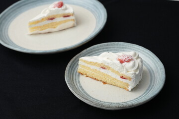 Small Japanese strawberry shortcakes on two stylish Japanese style plates, each on a black cloth on a white table.