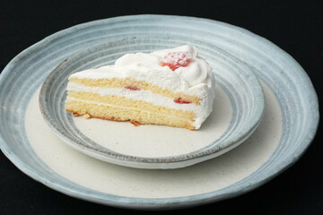 One small Japanese strawberry shortcake on two stylish overlapping large and small plates in Japanese style on a black cloth on a white table