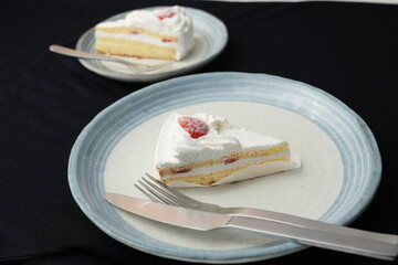 Small Japanese strawberry shortcake, fork and knife each on two stylish Japanese-style large and small plates on a black cloth on a white table