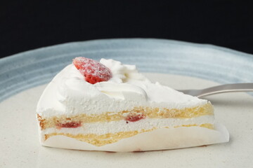 A small Japanese strawberry shortcake and a fork each on two stylish Japanese-style large and small plates on a black cloth on a white table