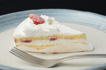 A small Japanese strawberry shortcake and a fork each on two stylish Japanese-style large and small plates on a black cloth on a white table