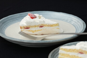 A small Japanese strawberry shortcake and a fork each on two stylish Japanese-style large and small plates on a black cloth on a white table