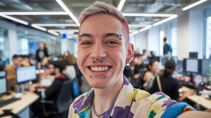 Fototapeta premium A cheerful young male with dyed hair and piercings smiles widely in a busy office environment filled with colleagues working at their desks.