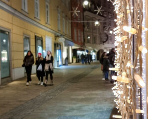 People walking on a street with beautiful Christmas decorations at night, in the city center of Graz, Styria region, Austria. Selective focus