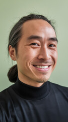 Fototapeta premium Smiling East Asian man in a black turtleneck, showcasing a friendly demeanor against a soft green background.