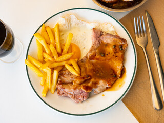 Hearty dish of European cuisine - two juicy fried pork chops with bone, supplemented with slices of French fries, fried egg and bran bread