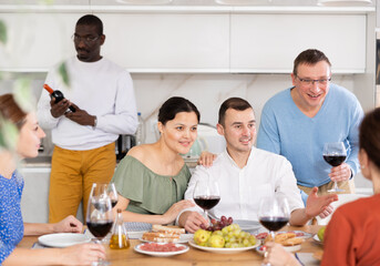 Multiethnic women and men friends talking and drinking wine in the kitchen