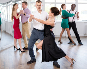 Dynamic young male and female attendees of dancing courses doing waltz in group