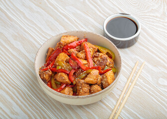 Chicken stir fry with red and green bell peppers sprinkled with sesame seeds, served in bowl, with chopsticks and soy sauce aside, composing a delicious asian meal