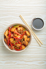 Chicken stir fry with red and green bell peppers sprinkled with sesame seeds, served in bowl, with chopsticks and soy sauce aside, composing a delicious asian meal