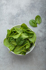 Fresh spinach leaves in a white bowl set on a gray backdrop, showcasing their vibrant green color...
