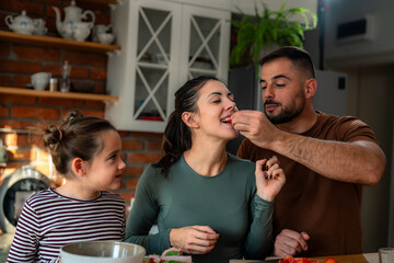 Family members take turns offering healthy bites to one another as they make breakfast in their home.