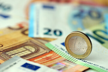 One euro coin lies on huge amount of different euro dollars banknotes