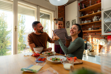 Family members take turns offering healthy bites to one another as they make breakfast in their home.