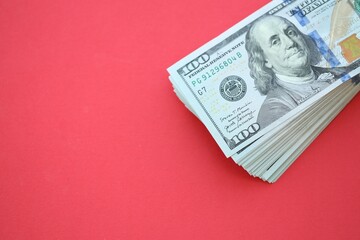 Big amount of hundred dollar bills in thick stack lies on bright red color paper background