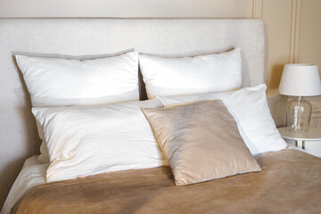 A neatly arranged bed features multiple fluffy white pillows and a soft taupe throw blanket. A...