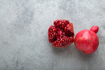 One whole and one half ripe pomegranate fruit showing juicy red seeds are laying on gray textured...