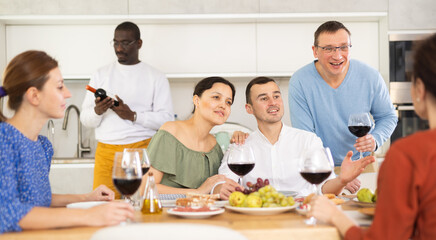 Multicultural female and male friends chatting and drinking wine at table