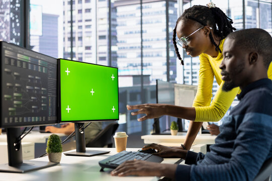Admin doing software debugging on isolated screen PC, asking for help from coworker, checking errors in lines of code. Worker fixing coding mistakes on chroma key computer, being assisted by colleague