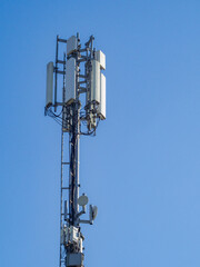 Cellular base station tower with antennas and microwave dishes providing wireless communication services against a clear blue sky ensures seamless connectivity