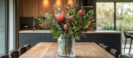 Fototapeta premium Native Australian foliage arranged artistically in a glass vase displayed on a rustic timber kitchen table