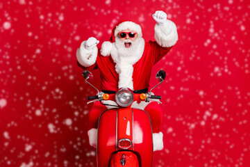 Photo of retired grandfather white beard cheerful ride retro moped raise fists open mouth win newyear deer racing bet wear x-mas costume coat sunglass cap isolated red color background