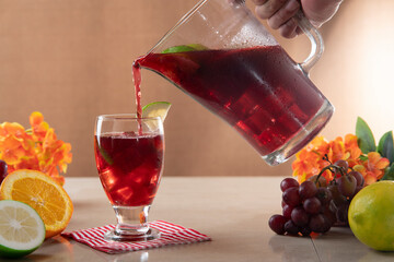 Close-up of glass carafe with homemade summer wine filling a glass surrounded by oranges, lemons and grapes on ceramic table