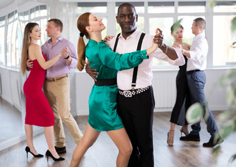 Fototapeta premium During rehearsal of reporting concert, woman with African-American man participants of dance workshop perform figure waltz. Group training and rehearsal, preparation for competitions