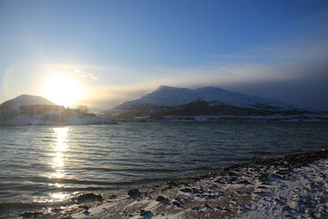 Fototapeta premium Winter landscapes in Norway showcase serene snowy mountains, icy fjords, and peaceful coastal views. Capturing the beauty of snow-covered trees, quiet roads, and glowing sunsets creates a sense of cal
