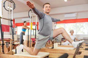 Man works out in gym on Pilates simulator. Sports club client performs exercise on reformer to...