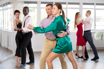 Fototapeta premium With unhurried music, man with woman in couple spins to rhythm of waltz during lesson for novice students. Classes in mini-groups for those who want to learn dancing