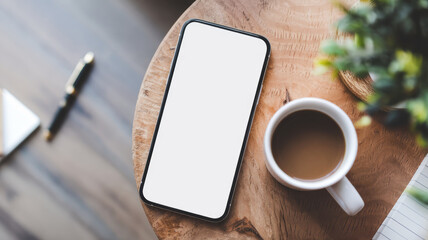 A phone and a cup of coffee sit on a wooden table. The phone is white and has a black case. The cup is white and has a brown liquid in it. The scene is simple and uncluttered