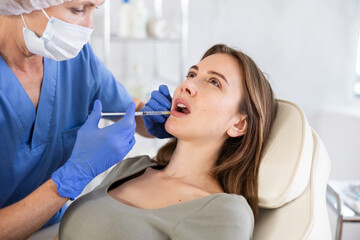 Young woman is getting a facial injections. She is lying calm. Cosmetologist is holding syringe.