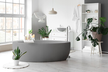 Bathtub and houseplants in light bathroom with panoramic windows