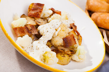 Delicious baked potatoes with cauliflower, fried bacon, mushrooms and cheese sauce