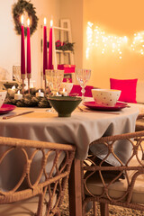 Festive table setting with burning candles and Christmas decorations in dining room at evening