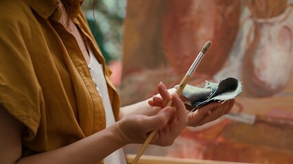 Female painter wiping off paint from paintbrush before mixing different colors, creating rustic...