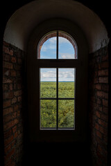 Sunlight streams through a window in a brick wall, revealing a breathtaking view of a lush green...