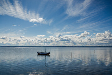 Small sailboat with furled sails peacefully sits on tranquil waters under a blue sky with fluffy clouds in chalupi, poland
