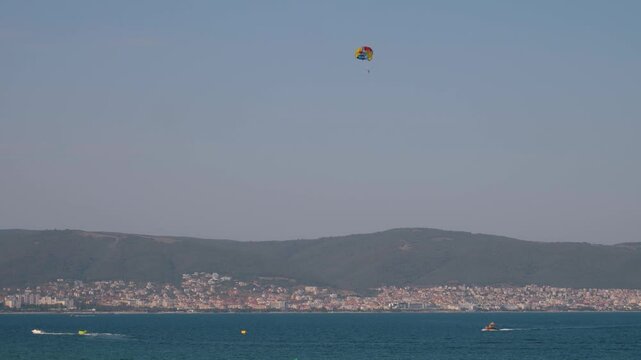 Experience thrill of parasailing above stunning coast, taking in vibrant blue sea and distant cityscape under clear sky. Soar through air and create unforgettable memories in this beautiful setting