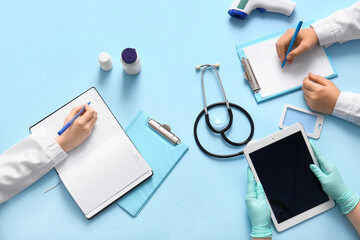 Doctor's hands writing in clipboard and holding tablet on blue background