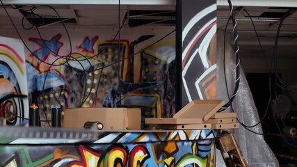 Close up of pizza boxes leftover by teenagers in city suburb abandoned building with graffiti art on walls. Vandalized location left in messy state by unlawful teens, concept of urban culture