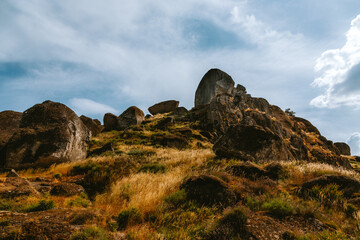 Monsanto, portugal, reveals its unique landscape with imposing megalithic boulders scattered across a hill covered in dry grass under a summer sky dotted with clouds