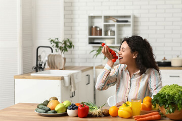 Young happy African-American woman with glass of juice, different vegetables and fruits in kitchen. Independence from Meat Day