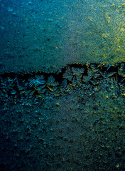 Close-up of intricate frost patterns on glass with a yellow and blue color gradient, resembling...