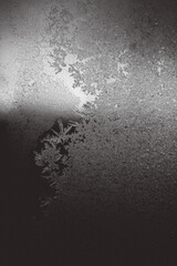 Detailed frost patterns and ice crystals on a glass surface, forming intricate textures in monochrome with soft light and shadow. Winter abstract background with natural beauty.  
