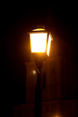 Close-up of a glowing vintage street lamp at night against a dark background, with a historic...