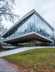 Fototapeta premium Modern architectural building with glass facade and sloping roof surrounded by trees.