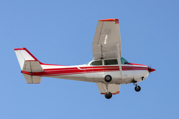 Aircraft low altitude fly by. Red and white general aviation airplane used for travel, training, and recreation. Fixed gear, high wings, and propeller powered. Isolated on blue sky